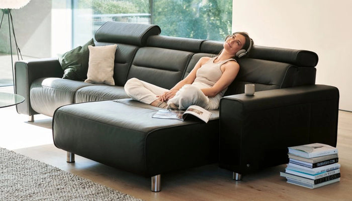 A woman sitting on an L shaped black sofa, listening music